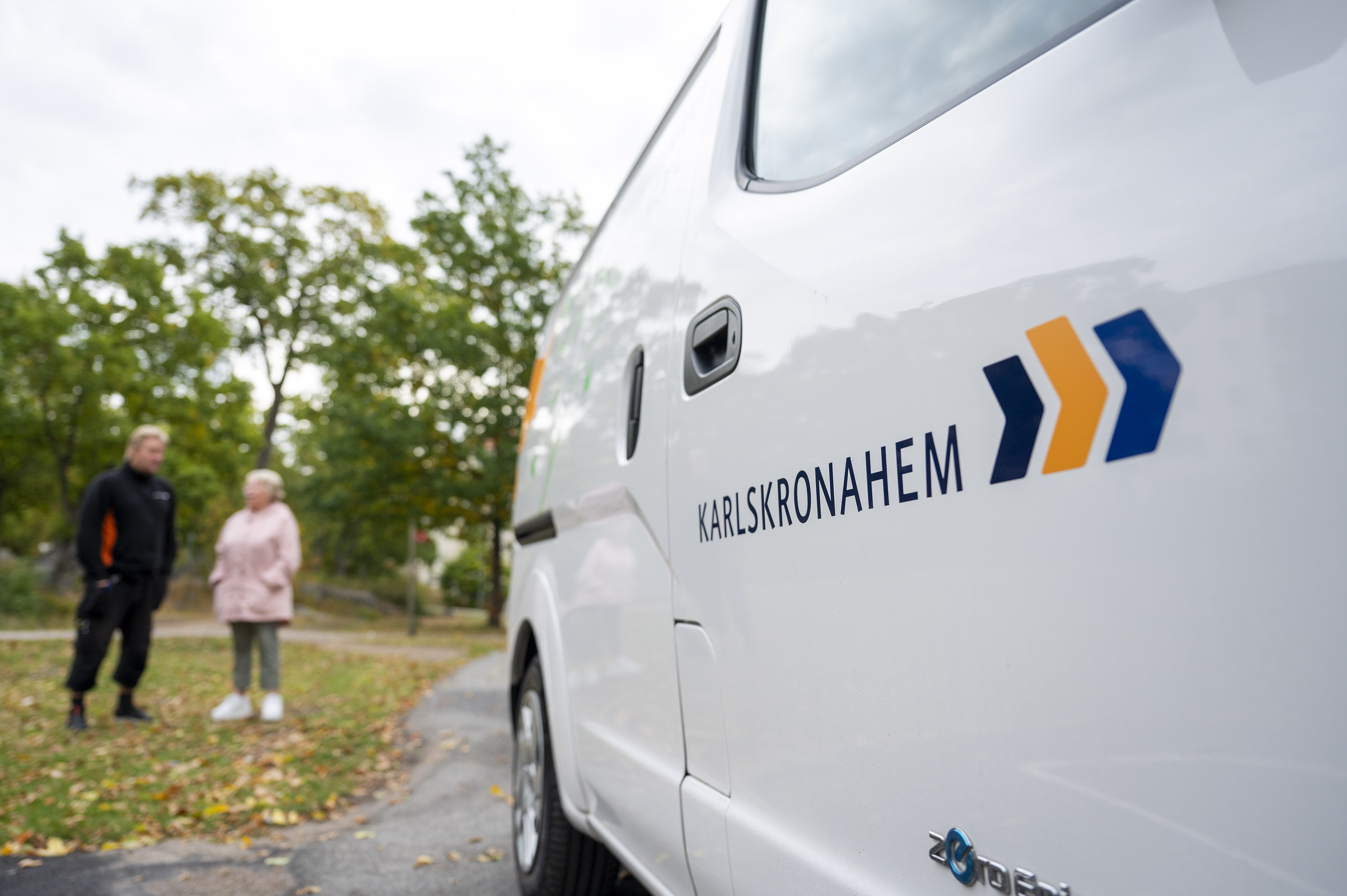 Karlskronahems servicebil parkerad i bostadsområde, med två personer i bakgrunden.